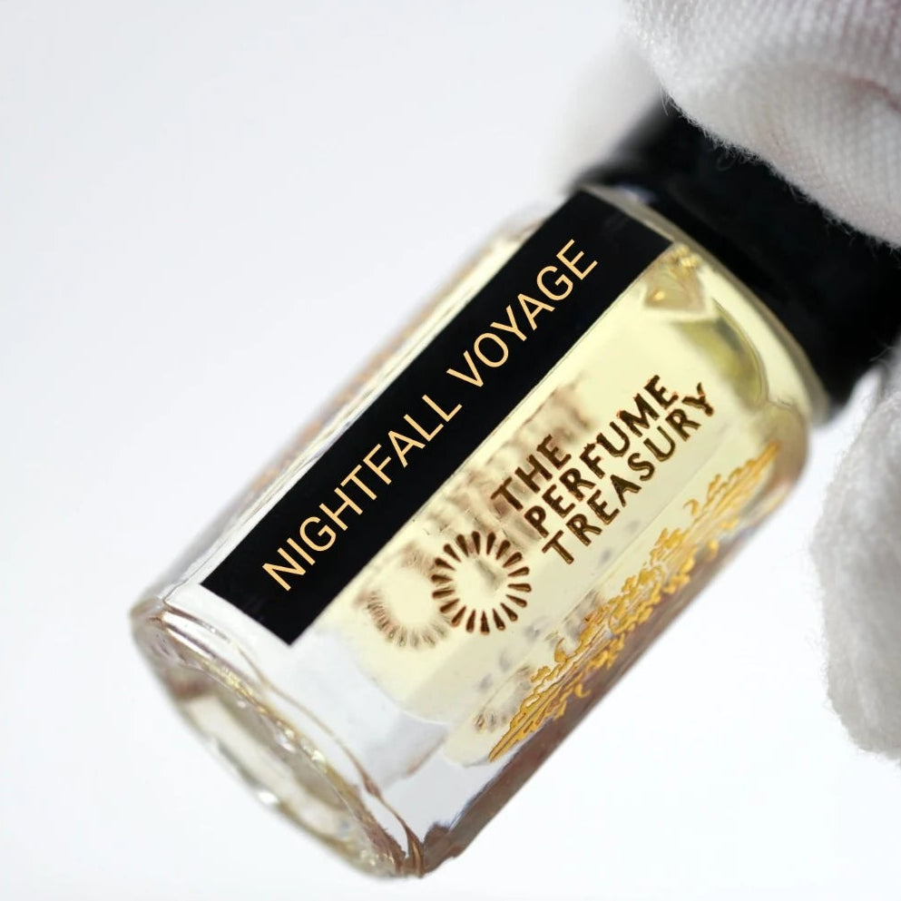 Close-up of Nightfall Voyage perfume oil by The Perfume Treasury held in a white glove, showing the black and gold label and pale golden fragrance oil.