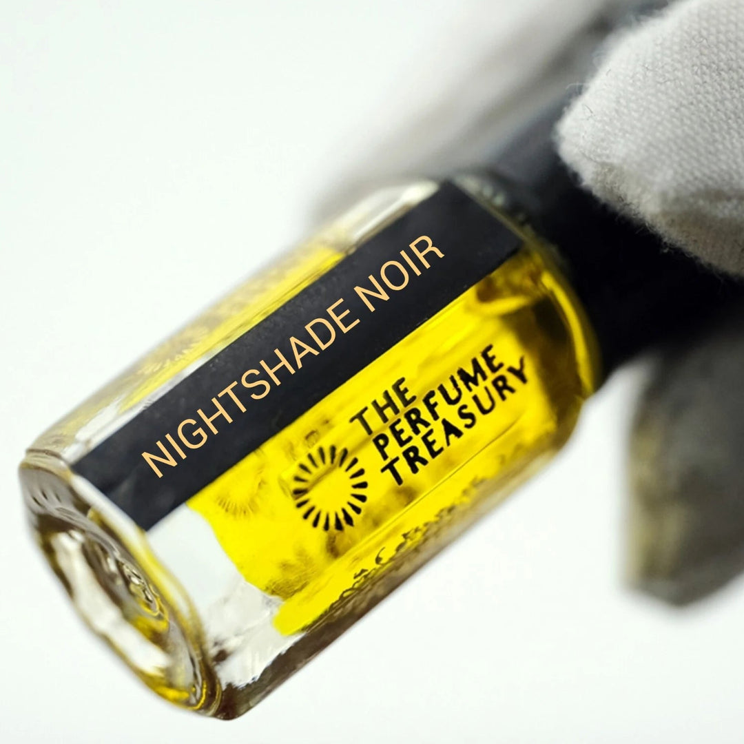 Close-up of Nightshade Noir perfume oil by The Perfume Treasury held in a white glove, showing the black and gold label and rich golden fragrance oil.