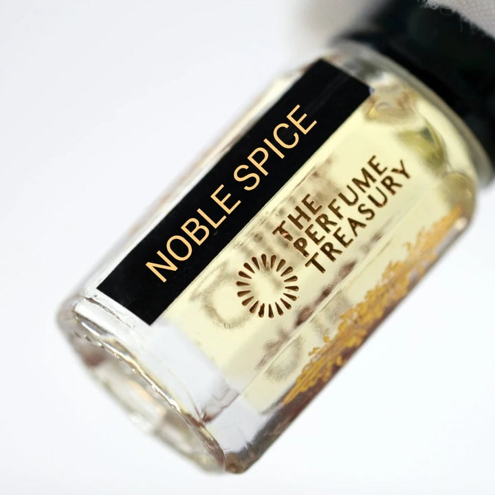 Close-up of Noble Spice perfume oil by The Perfume Treasury held in a white glove, showing the black and gold label and pale golden fragrance oil.