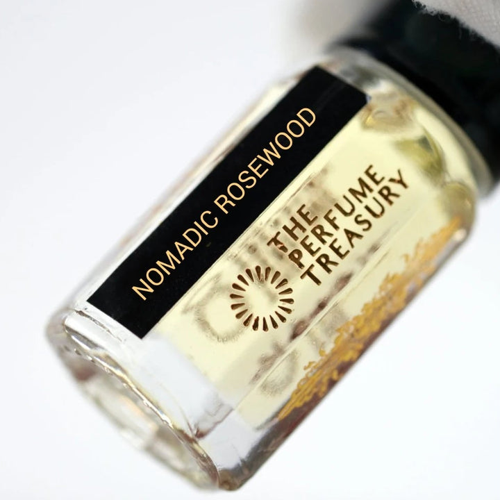 Close-up of Nomadic Rosewood perfume oil by The Perfume Treasury held in a white glove, showing the black and gold label and pale golden fragrance oil.