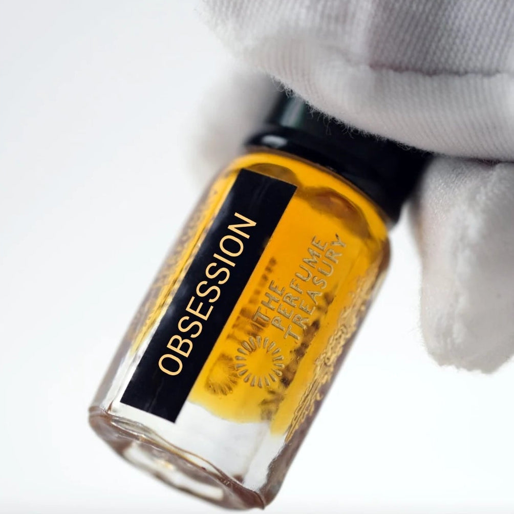 Close-up of Obsession perfume oil by The Perfume Treasury held in a white glove, showing the black and gold label and rich amber fragrance oil.