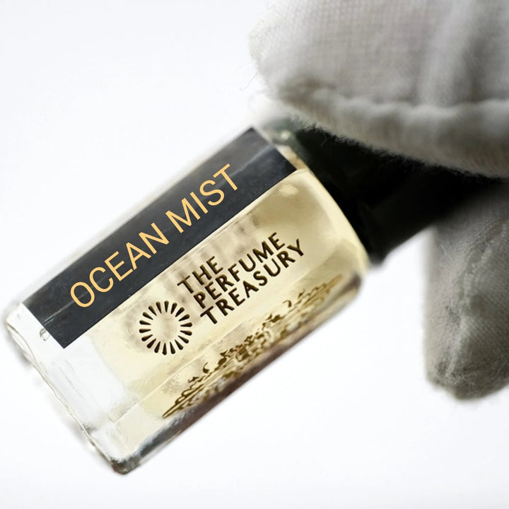 Close-up of Ocean Mist perfume oil by The Perfume Treasury held in a white glove, showing the black and gold label and pale golden fragrance oil.