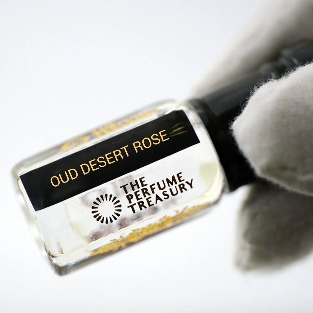 Close-up macro of Oud Desert Rose 3ml attar perfume oil bottle by The Perfume Treasury, showing clear slightly viscous fragrance oil and premium glass detail, luxury oil in clear bottle with black cap.
