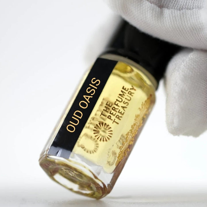 Oud Oasis perfume oil by The Perfume Treasury held in a white-gloved hand, showing the branded glass bottle and golden perfume oil.