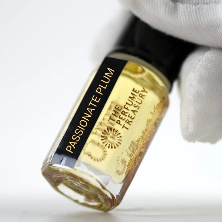 Passionate Plum perfume oil by The Perfume Treasury held in a white-gloved hand, showing the branded glass bottle and golden perfume oil.