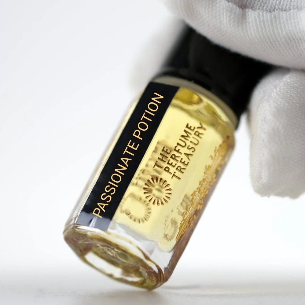Passionate Potion perfume oil by The Perfume Treasury held in a white-gloved hand, highlighting the branded bottle and golden perfume oil.