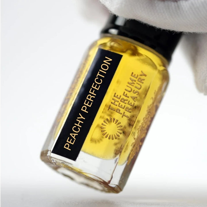 Peachy Perfection perfume oil by The Perfume Treasury held in a white-gloved hand, highlighting the golden perfume oil and branded bottle.