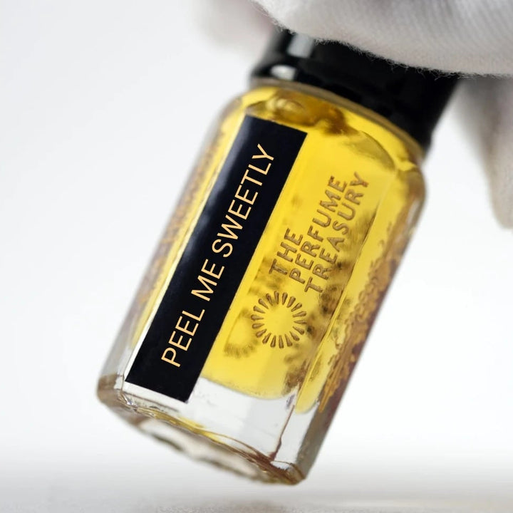 Peel Me Sweetly perfume oil by The Perfume Treasury held in a white-gloved hand, showing the golden perfume oil and branded bottle.