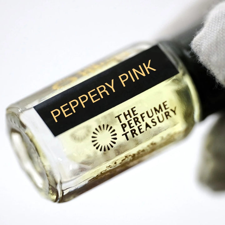 Peppery Pink perfume oil by The Perfume Treasury held in a white-gloved hand, highlighting the pale golden perfume oil and branded bottle.