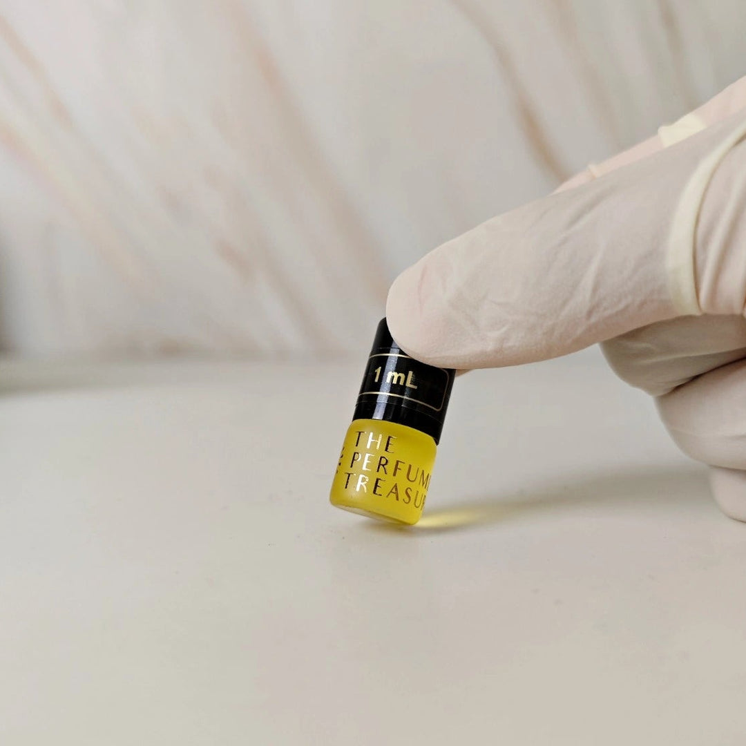 Small 1ml Frosted glass perfume oil bottle with black cap, attar perfume oil by The Perfume Treasury, golden fragrance oil held in white gloved hand on neutral background.