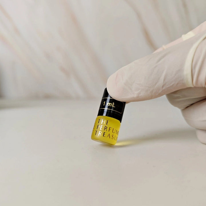 Small 1ml Frosted glass perfume oil bottle with black cap, attar perfume oil by The Perfume Treasury, golden fragrance oil held in white gloved hand on neutral background.