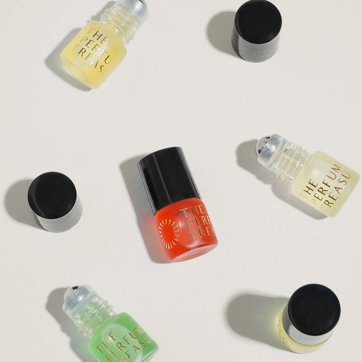 Flat lay of multiple perfume oil bottles by The Perfume Treasury, assorted coloured fragrance oils in small glass roll-on bottles with black caps on white background.