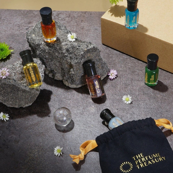 Perfume oil collection flat lay by The Perfume Treasury with luxury pouch, stones and flowers, showcasing multiple fragrance oils in a premium setting.