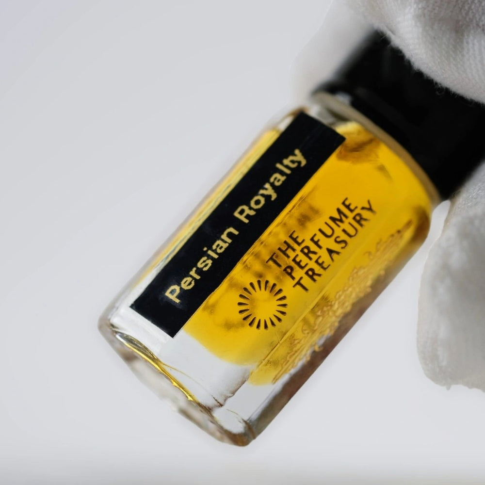 Close-up macro of Persian Royalty 3ml attar perfume oil bottle by The Perfume Treasury, showing rich amber golden oil and glossy texture, luxury fragrance oil in clear glass bottle.