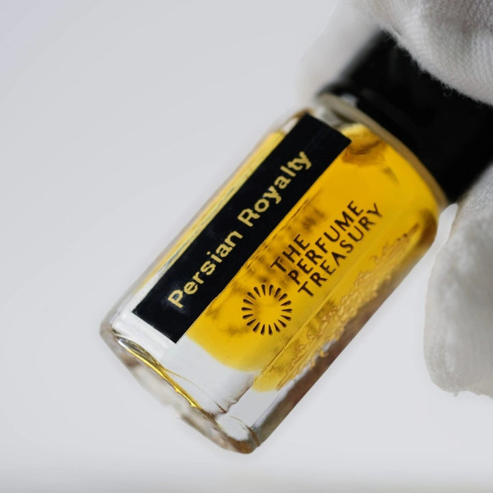 Close-up macro of Persian Royalty 3ml attar perfume oil bottle by The Perfume Treasury, showing rich amber golden oil and glossy texture, luxury fragrance oil in clear glass bottle.