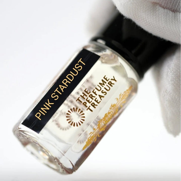 Pink Stardust perfume oil by The Perfume Treasury held in a white-gloved hand, showing the clear perfume oil and branded bottle.