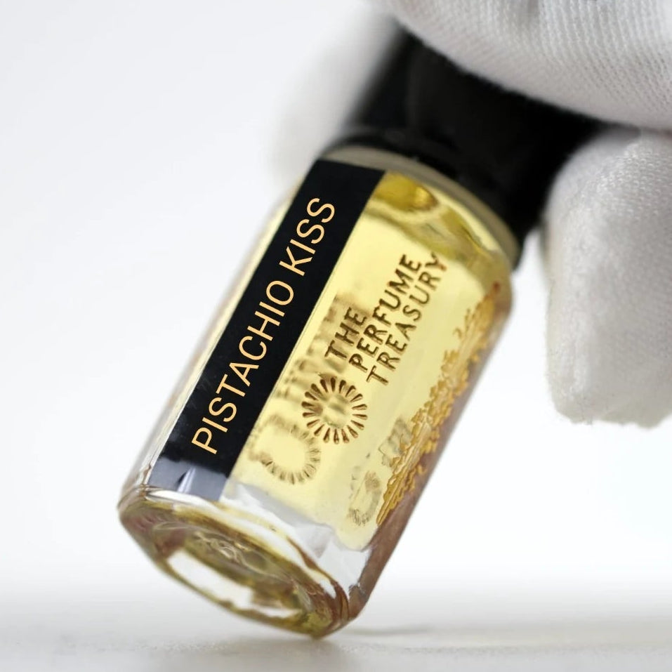 Pistachio Kiss perfume oil by The Perfume Treasury held in a white-gloved hand, highlighting the golden perfume oil and branded bottle.