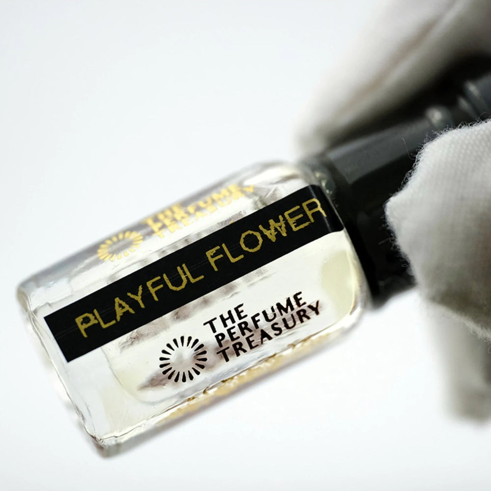 Playful Flower perfume oil by The Perfume Treasury held in a white-gloved hand, highlighting the clear perfume oil and branded bottle.