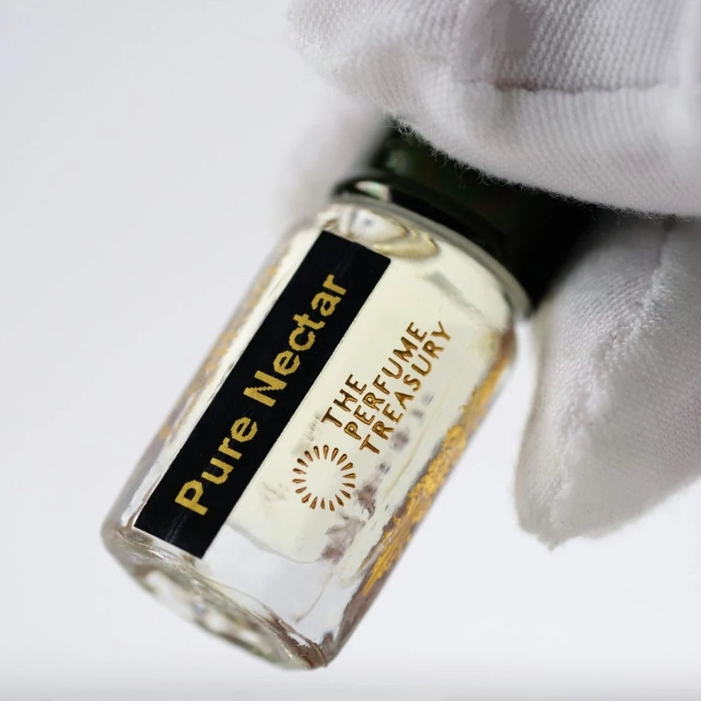 Pure Nectar perfume oil by The Perfume Treasury held in a white-gloved hand, highlighting the clear glass bottle and pale golden fragrance oil.