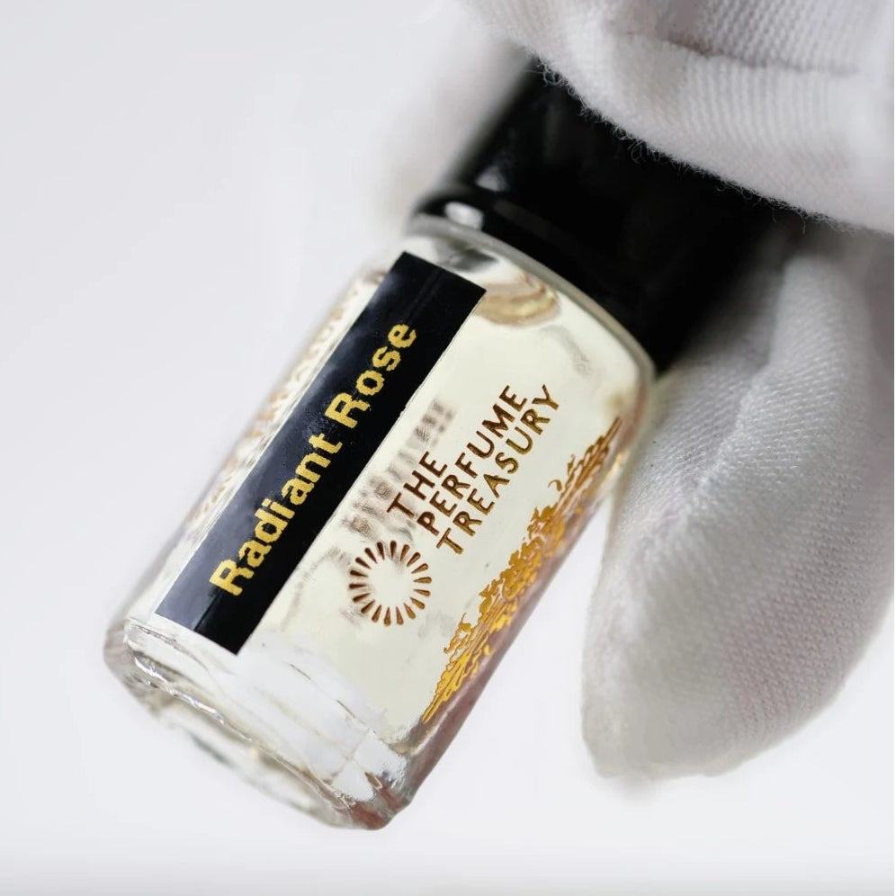 Radiant Rose perfume oil by The Perfume Treasury held in a white-gloved hand, highlighting the clear glass bottle and pale fragrance oil.