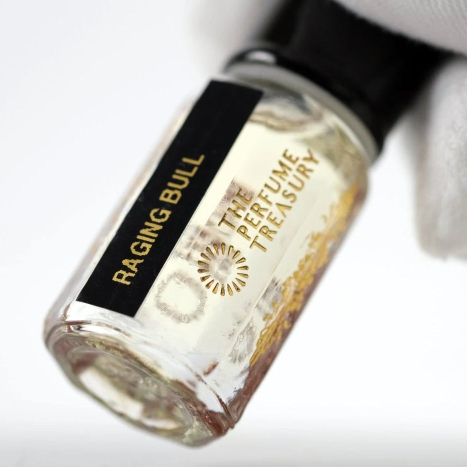 Raging Bull perfume oil by The Perfume Treasury held in a white-gloved hand, showing the clear glass bottle and pale fragrance oil.