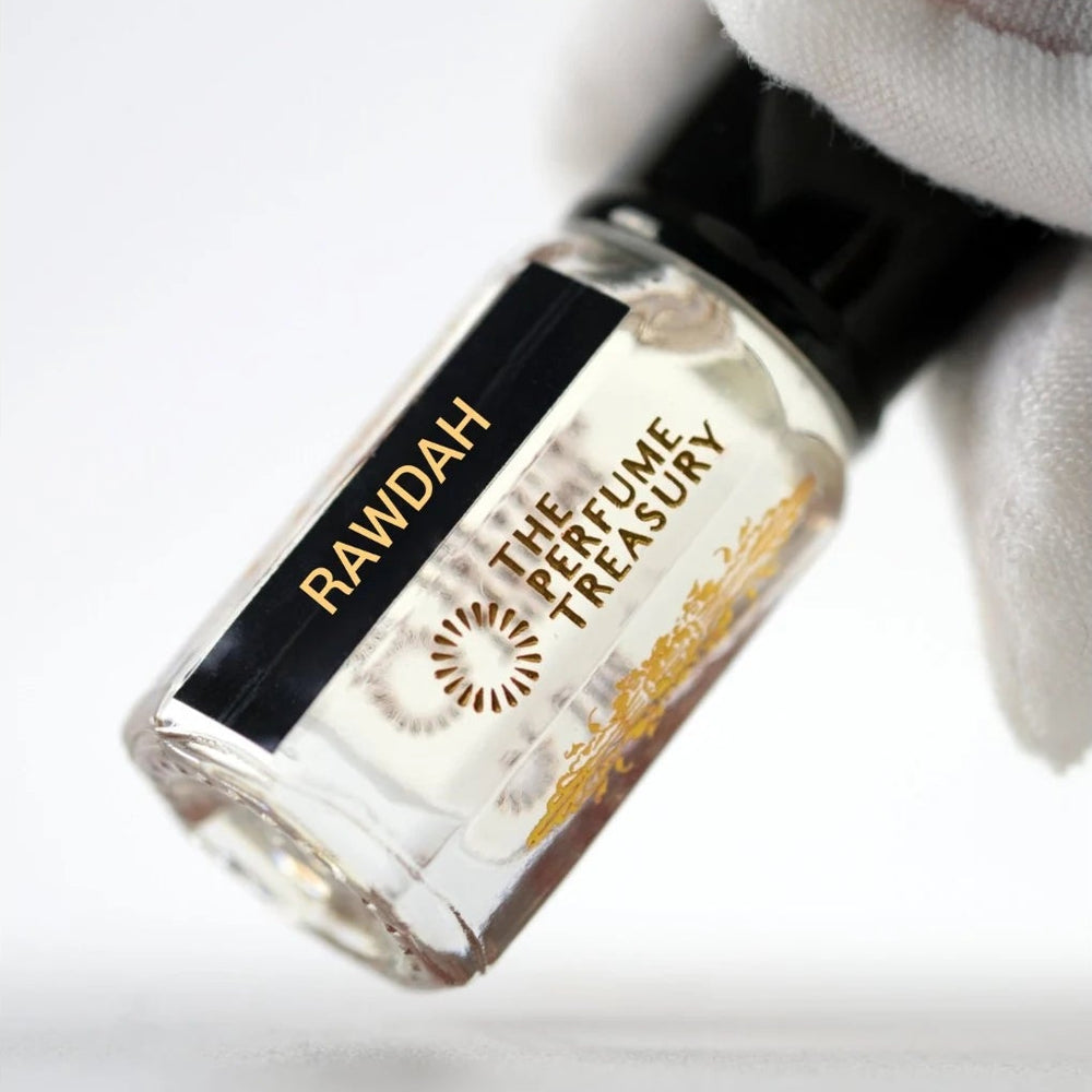Rawdah perfume oil by The Perfume Treasury held in a white-gloved hand, showing the clear glass bottle and pale fragrance oil.