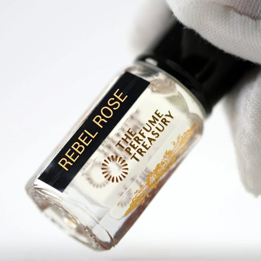 Rebel Rose perfume oil by The Perfume Treasury held in a white-gloved hand, showing the clear glass bottle and pale fragrance oil.