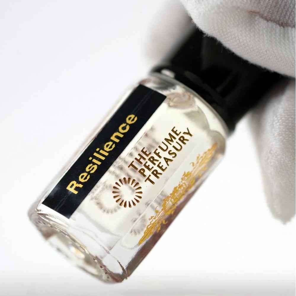Resilience perfume oil by The Perfume Treasury held in a white-gloved hand, highlighting the clear glass bottle and pale fragrance oil.