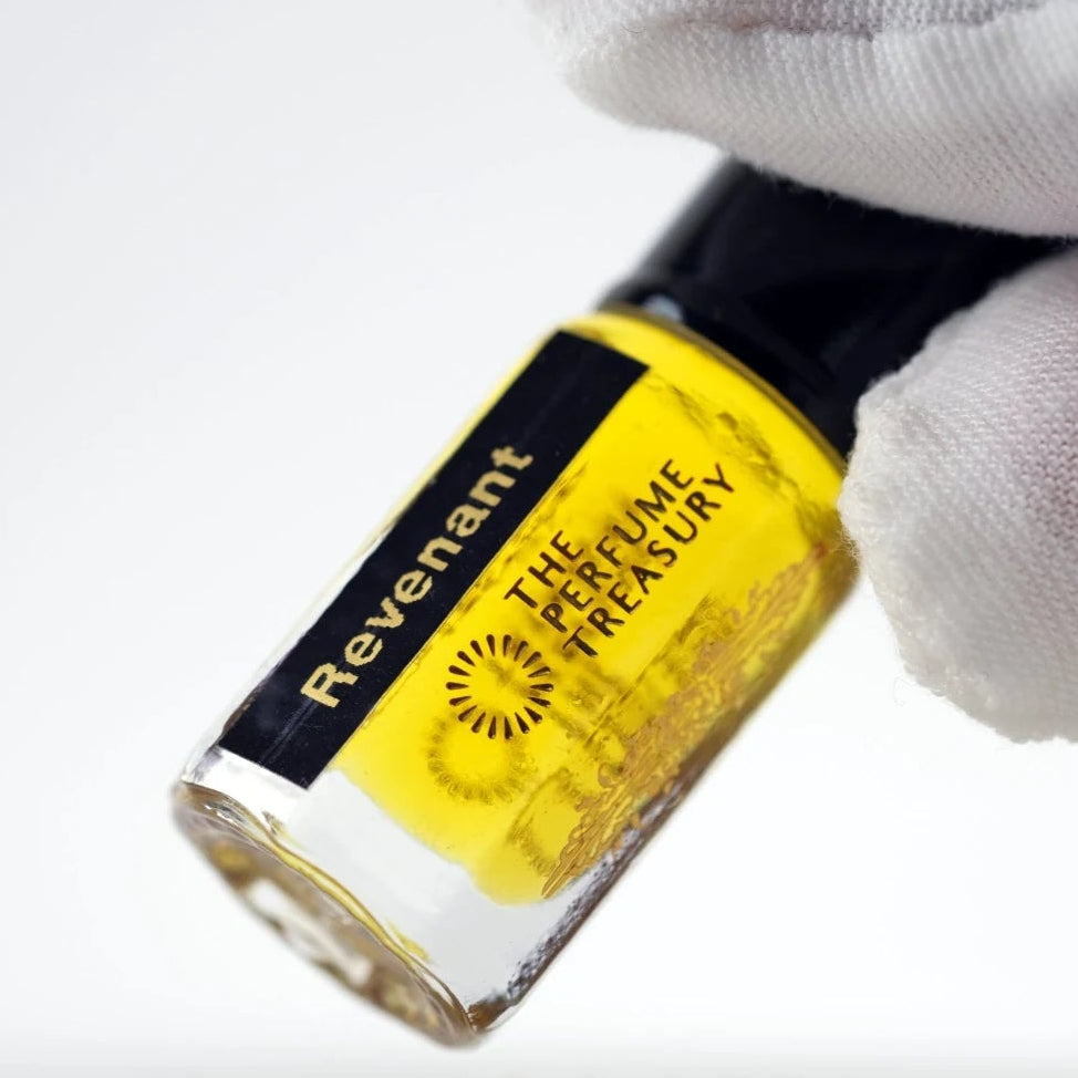 Revenant perfume oil by The Perfume Treasury held in a white-gloved hand, showing the rich golden fragrance oil.
