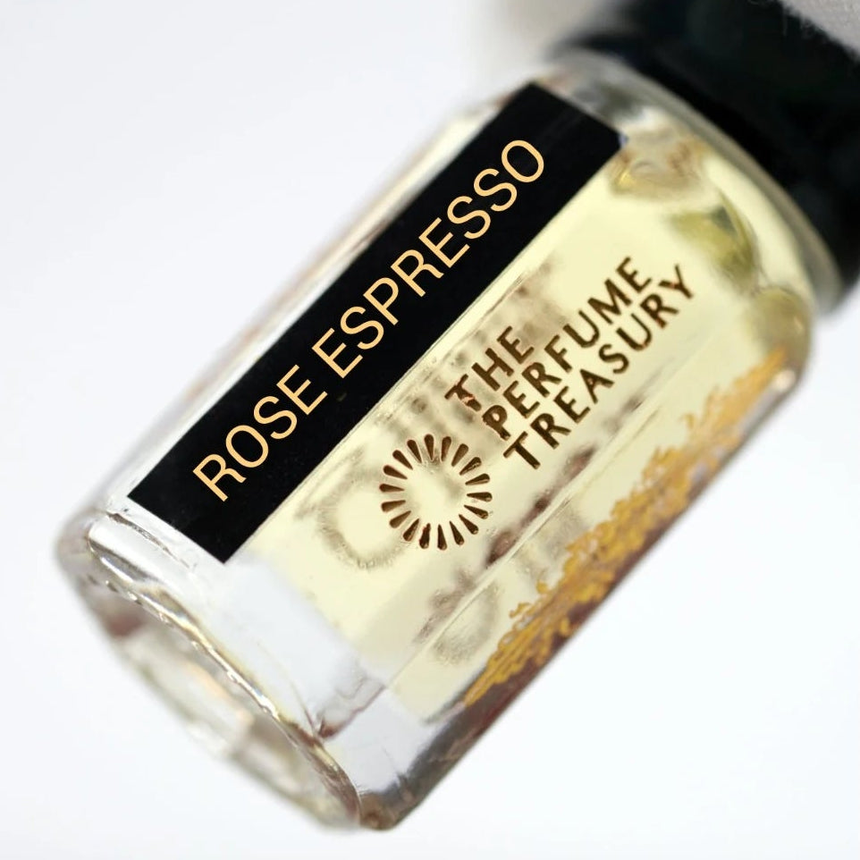 Rose Espresso perfume oil by The Perfume Treasury held in a white-gloved hand, highlighting the clear glass bottle and pale golden fragrance oil.