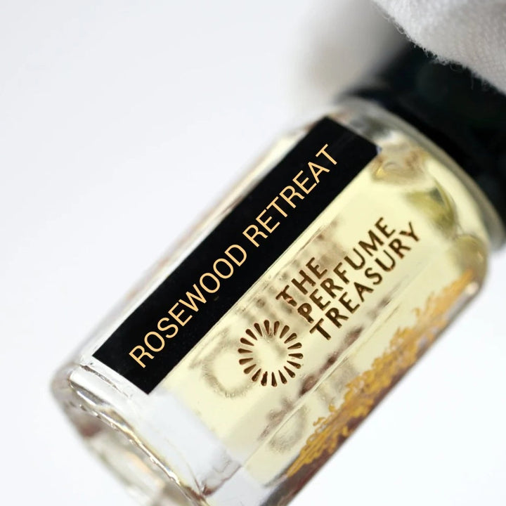 Rosewood Retreat perfume oil by The Perfume Treasury held in a white-gloved hand, showing the clear glass bottle and pale golden fragrance oil.