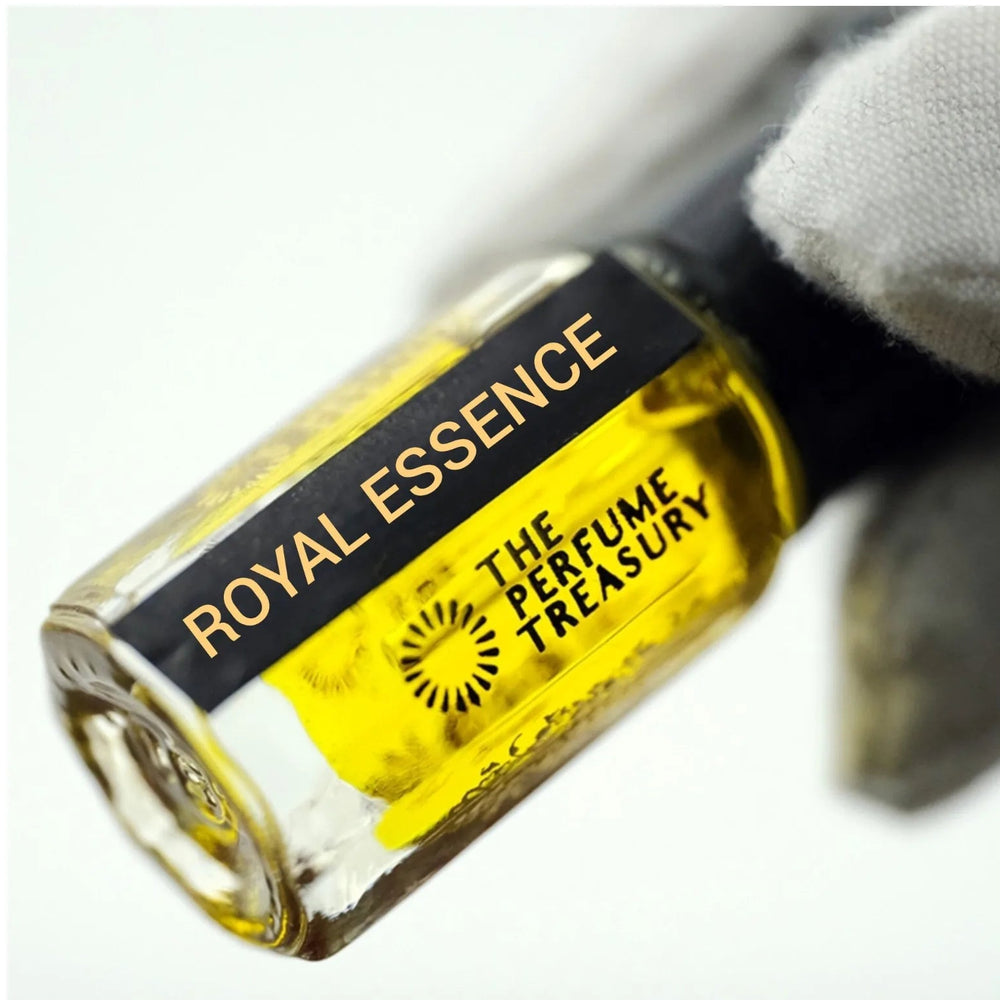 Close-up macro of Royal Essence 3ml attar perfume oil bottle held with white glove by The Perfume Treasury, showing vibrant golden fragrance oil and glossy glass detail, luxury perfume oil.
