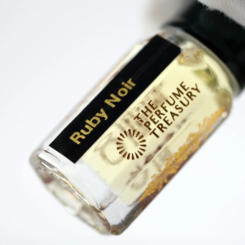Ruby Noir perfume oil by The Perfume Treasury held in a white-gloved hand, highlighting the clear glass bottle and pale golden fragrance oil.