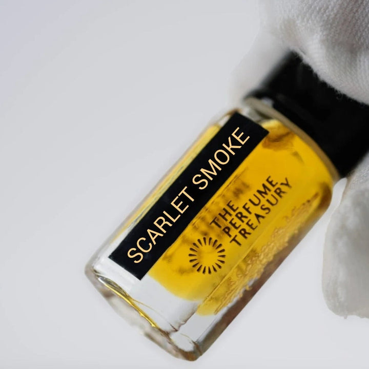 Scarlet Smoke perfume oil by The Perfume Treasury held in a white-gloved hand, showing the clear glass bottle and rich amber fragrance oil.