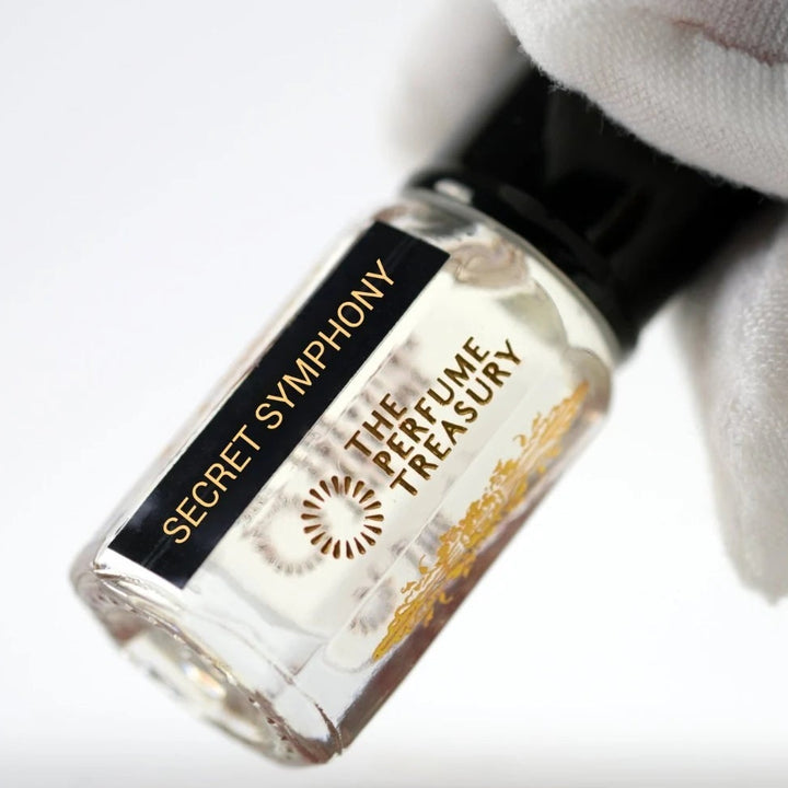 Secret Symphony perfume oil by The Perfume Treasury held in a white-gloved hand, highlighting the clear glass bottle and elegant branding.