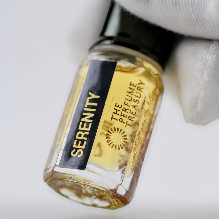 Serenity perfume oil by The Perfume Treasury held in a white-gloved hand, highlighting the golden fragrance oil and black label.