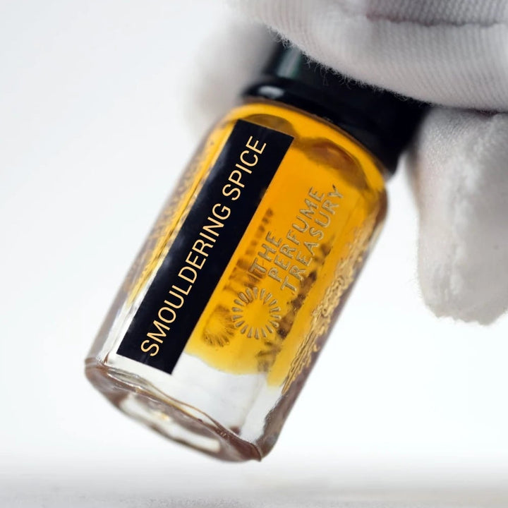 Smouldering Spice perfume oil in a clear glass bottle filled with rich amber golden fragrance oil, with a glossy black lid and black gold label, held by a white-gloved hand