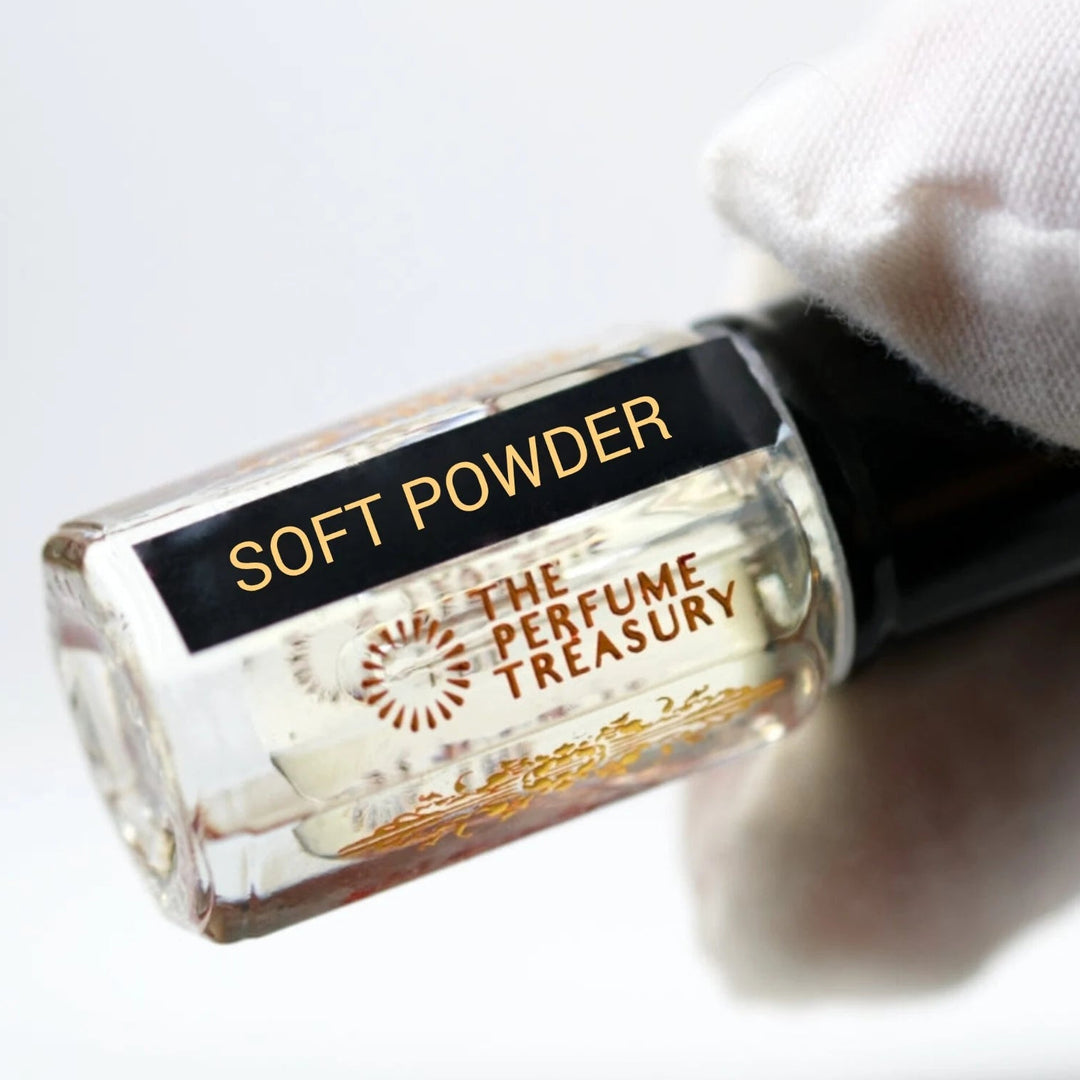 Soft Powder perfume oil by The Perfume Treasury in a clear glass bottle with pale fragrance oil, glossy black lid and black gold label, held horizontally by a white-gloved hand against a bright white background