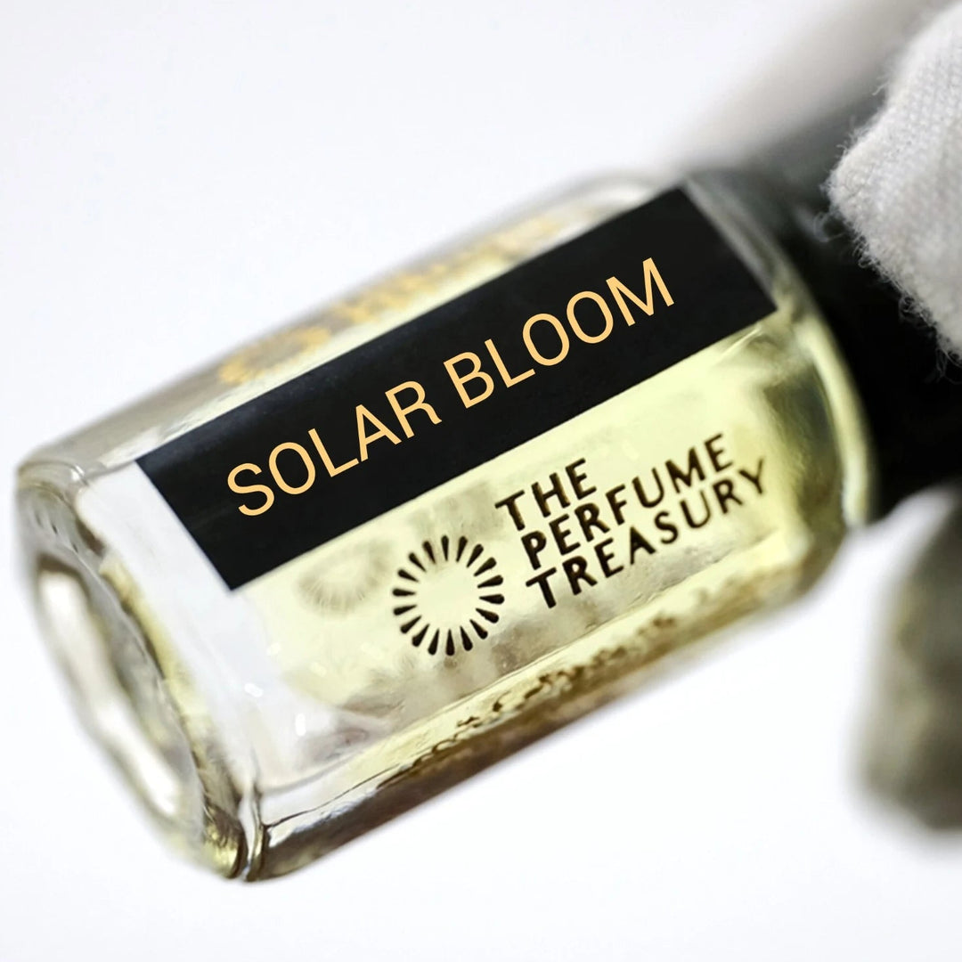 Solar Bloom perfume oil by The Perfume Treasury in a clear glass bottle with pale golden fragrance oil, glossy black lid and black gold label, held horizontally by a white-gloved hand