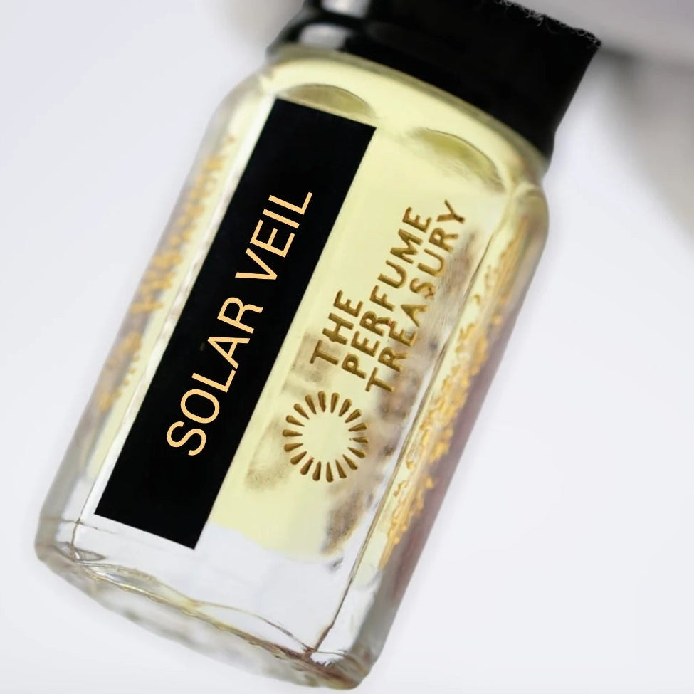 Solar Veil perfume oil by The Perfume Treasury in a clear glass bottle with pale golden fragrance oil, glossy black lid and black gold label, held at an angle against a clean white background