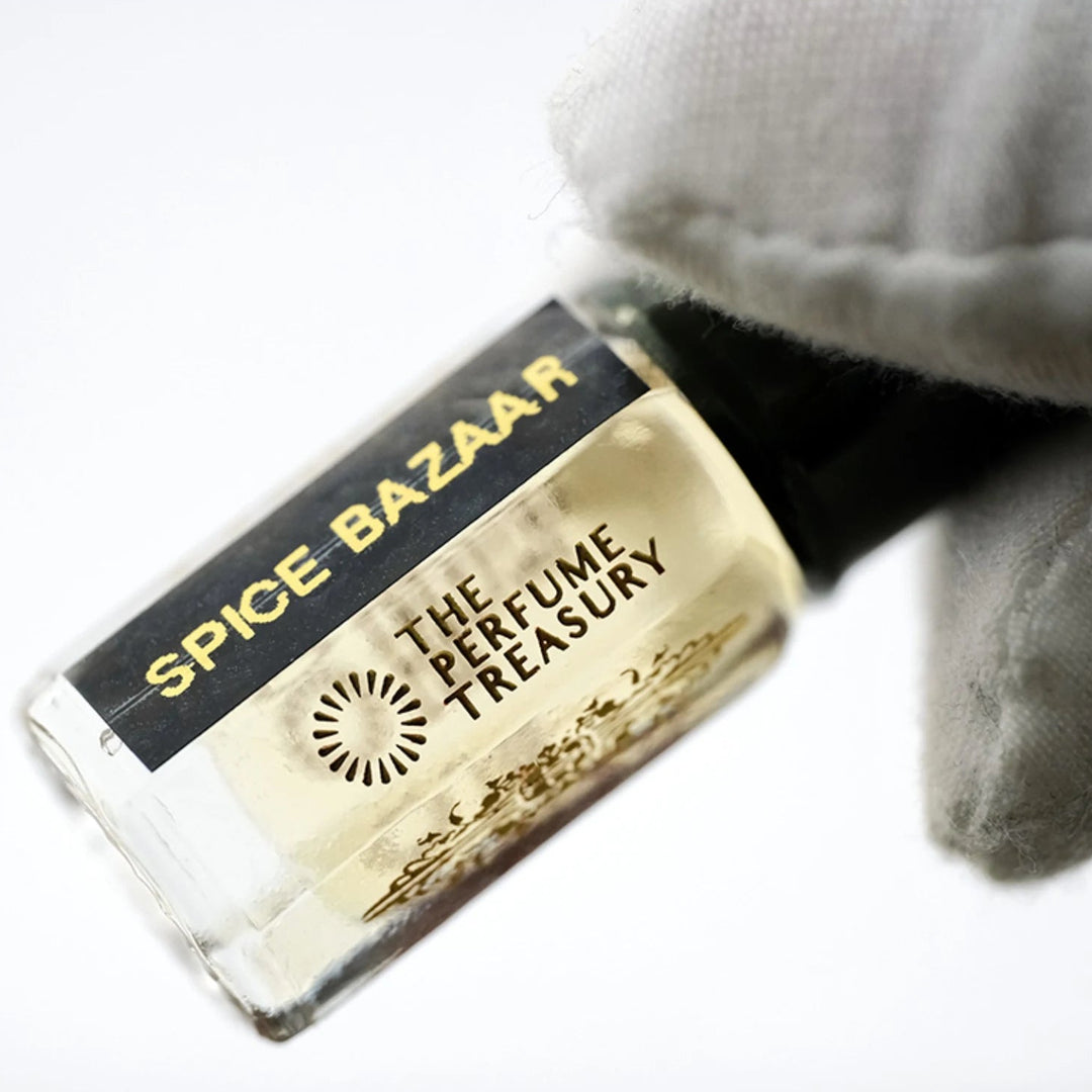 Spice Bazaar perfume oil by The Perfume Treasury in a clear glass bottle with golden fragrance oil, glossy black lid and black gold label, held at an angle by a white-gloved hand