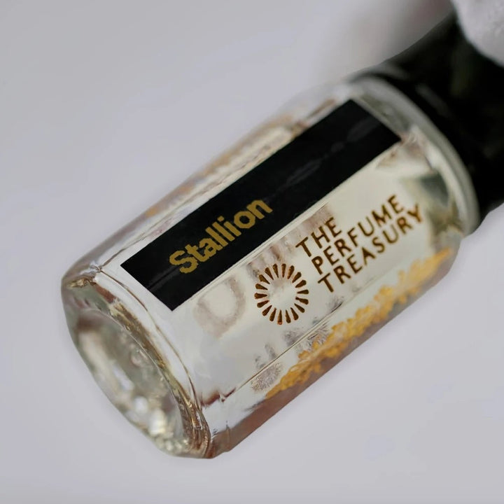 Stallion perfume oil by The Perfume Treasury in a clear glass bottle with black lid and black gold label, held at an angle by a white-gloved hand against a clean background
