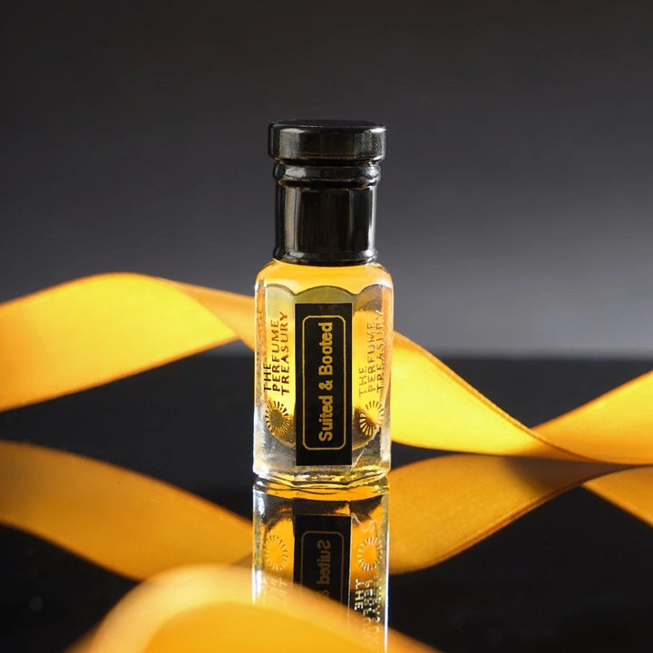 Suited &amp; Booted perfume oil by The Perfume Treasury displayed against a sophisticated black background with flowing gold fabric and a reflective surface for a luxurious elegant aesthetic