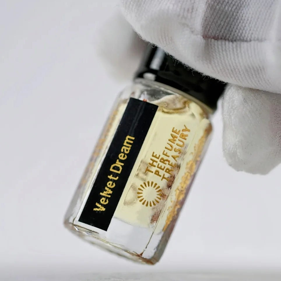 Close-up macro of Velvet Dream 3ml attar perfume oil bottle held with white glove by The Perfume Treasury, showing light creamy fragrance oil and glass detail, luxury perfume oil.