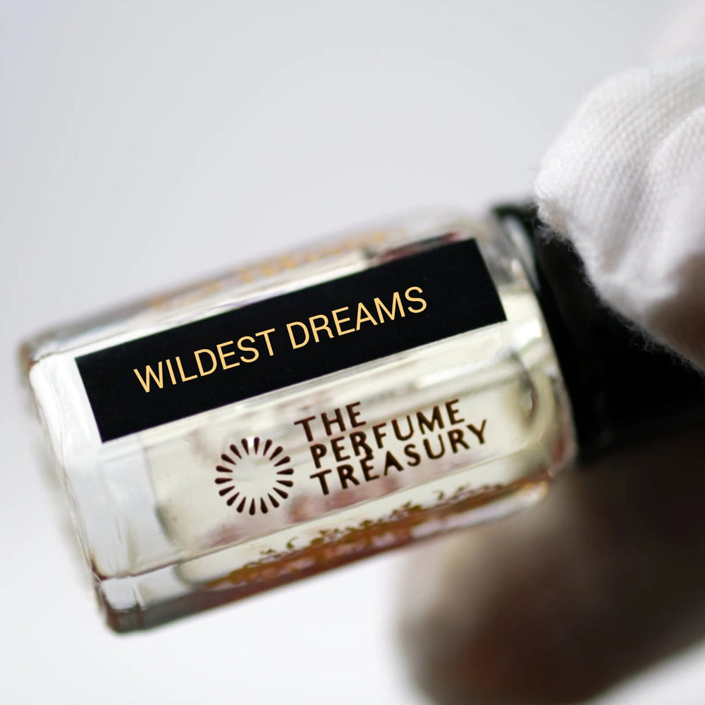 Close-up macro of Wildest Dreams 3ml attar perfume oil bottle by The Perfume Treasury, showing clear smooth fragrance oil texture and glass clarity, luxury oil in clear bottle with black cap.