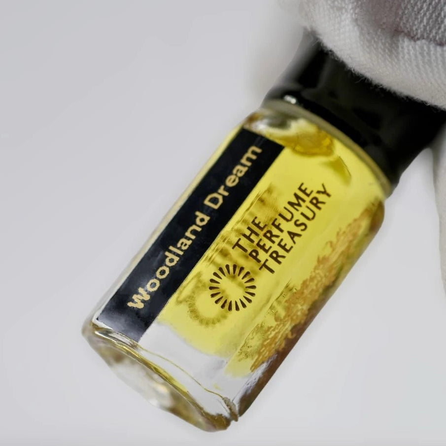 Close-up of Woodland Dream attar perfume oil bottle held with white glove by The Perfume Treasury, showcasing golden fragrance oil and luxury finish.