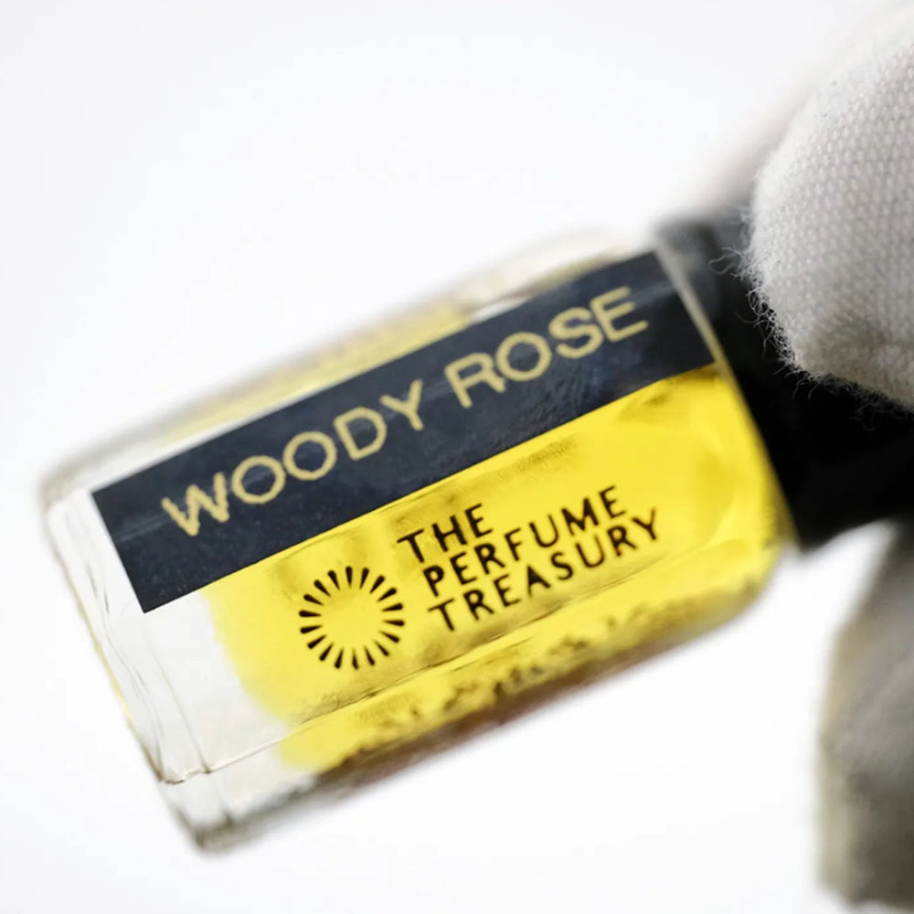 Close-up macro of Woody Rose 3ml attar perfume oil bottle held with white glove by The Perfume Treasury, showing rich golden oil and glass detail, luxury perfume oil.